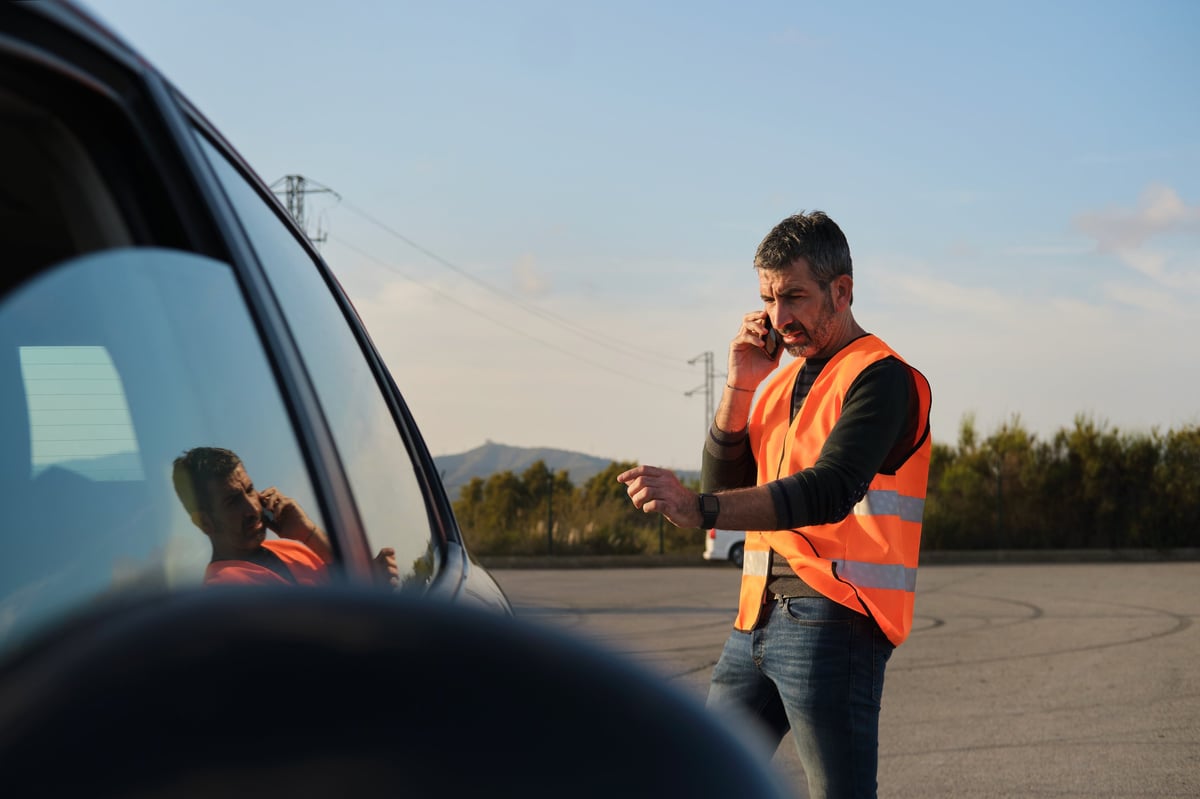 side view portrait of a European generation x man near a road explaining some broken car issues talking by the phone waiting to the car tow truck at sunset view