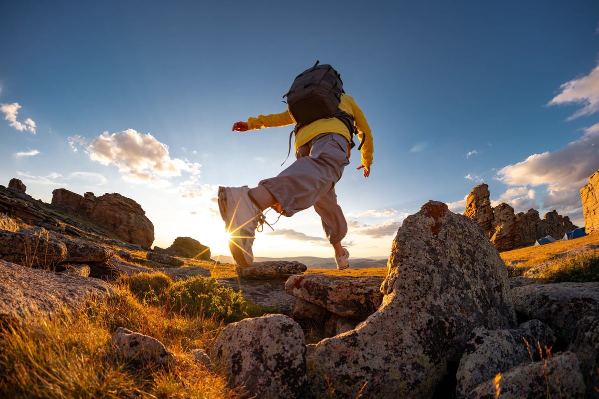 Female hiker jumping from rock to rock at sunset mountain top