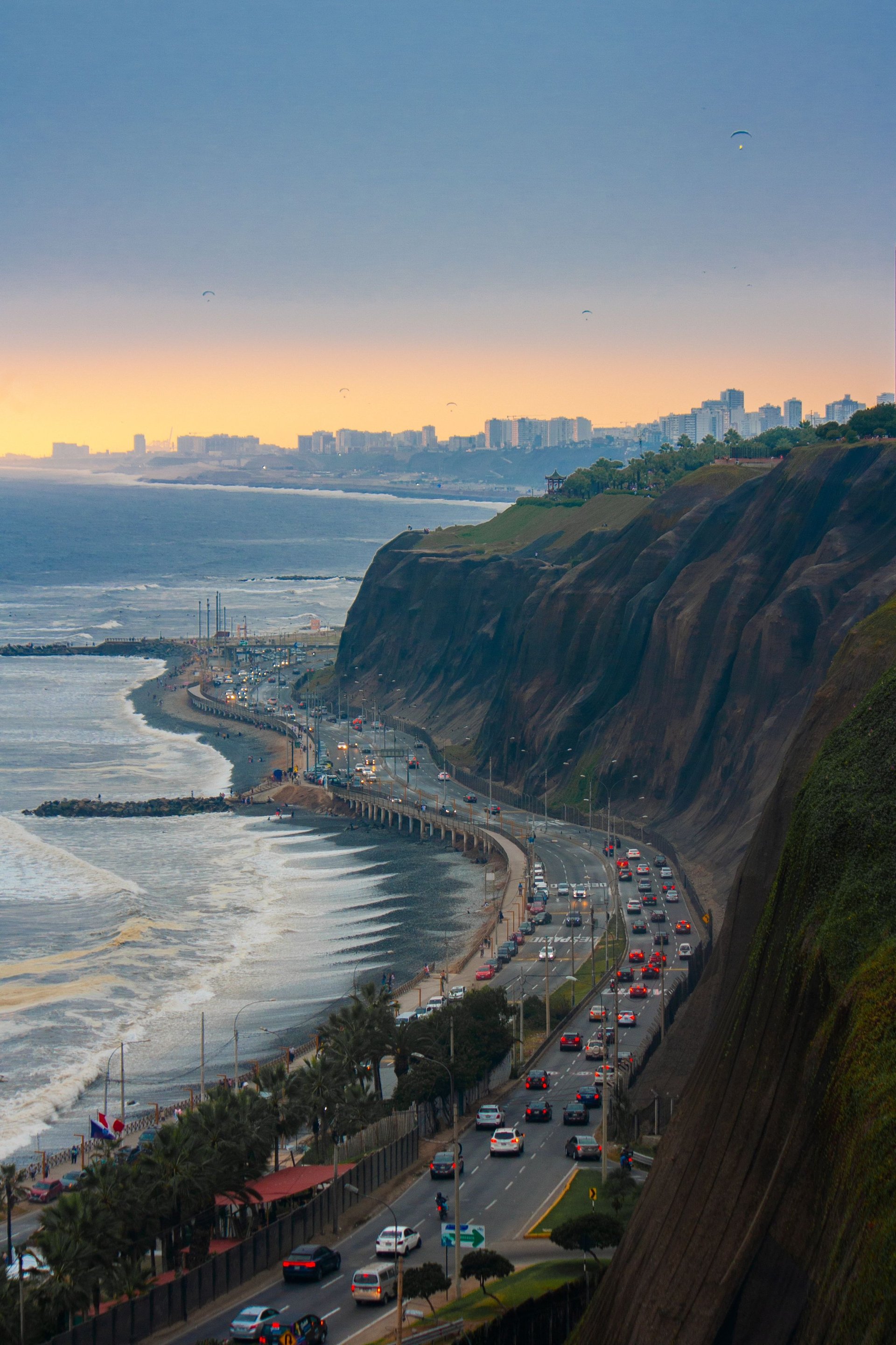 Coastal city skyline at sunset with tall cliffs, beach, ocean, palm trees